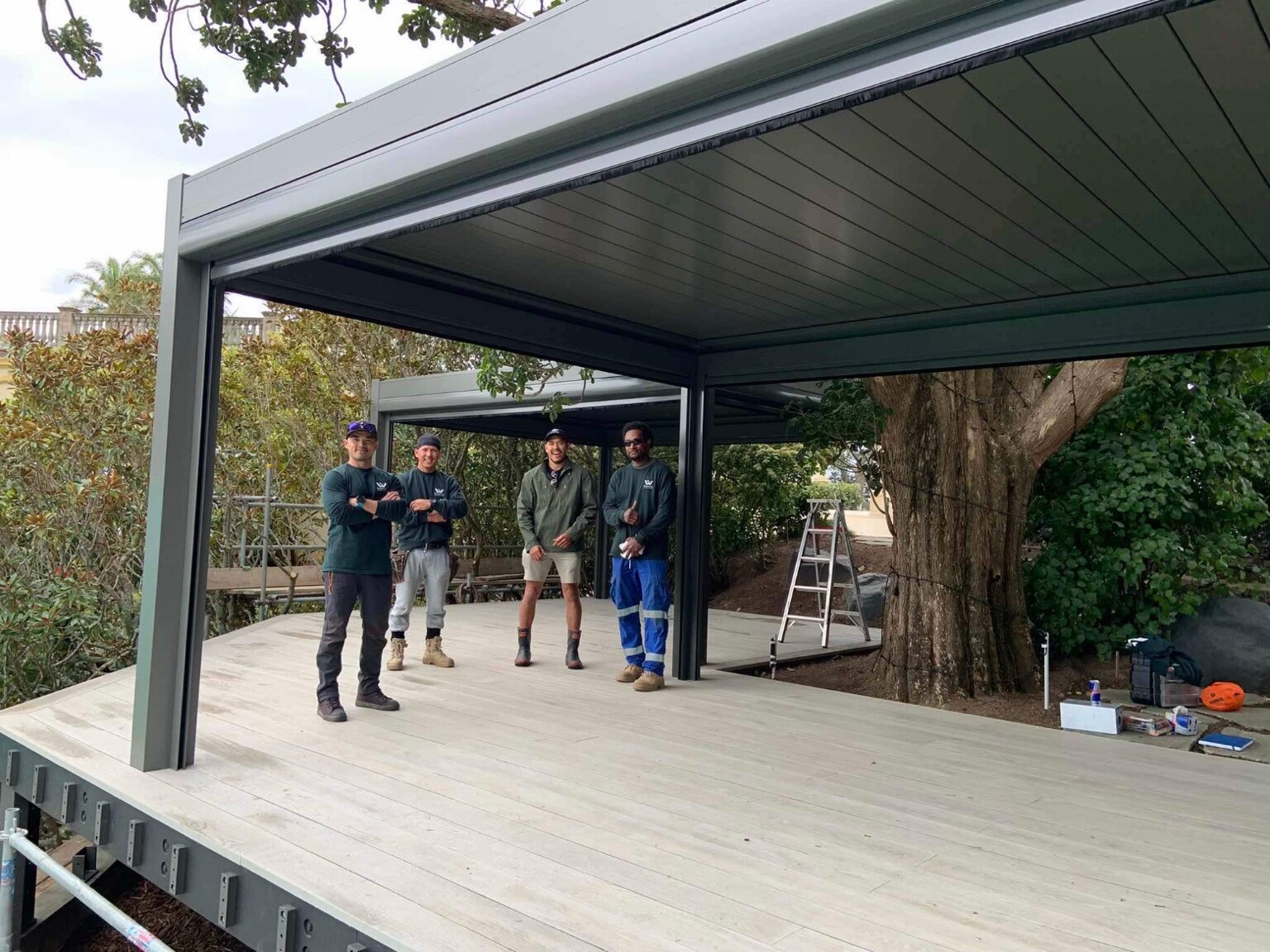GRIT team standing beneath completed louvre roofs on a large timber deck
