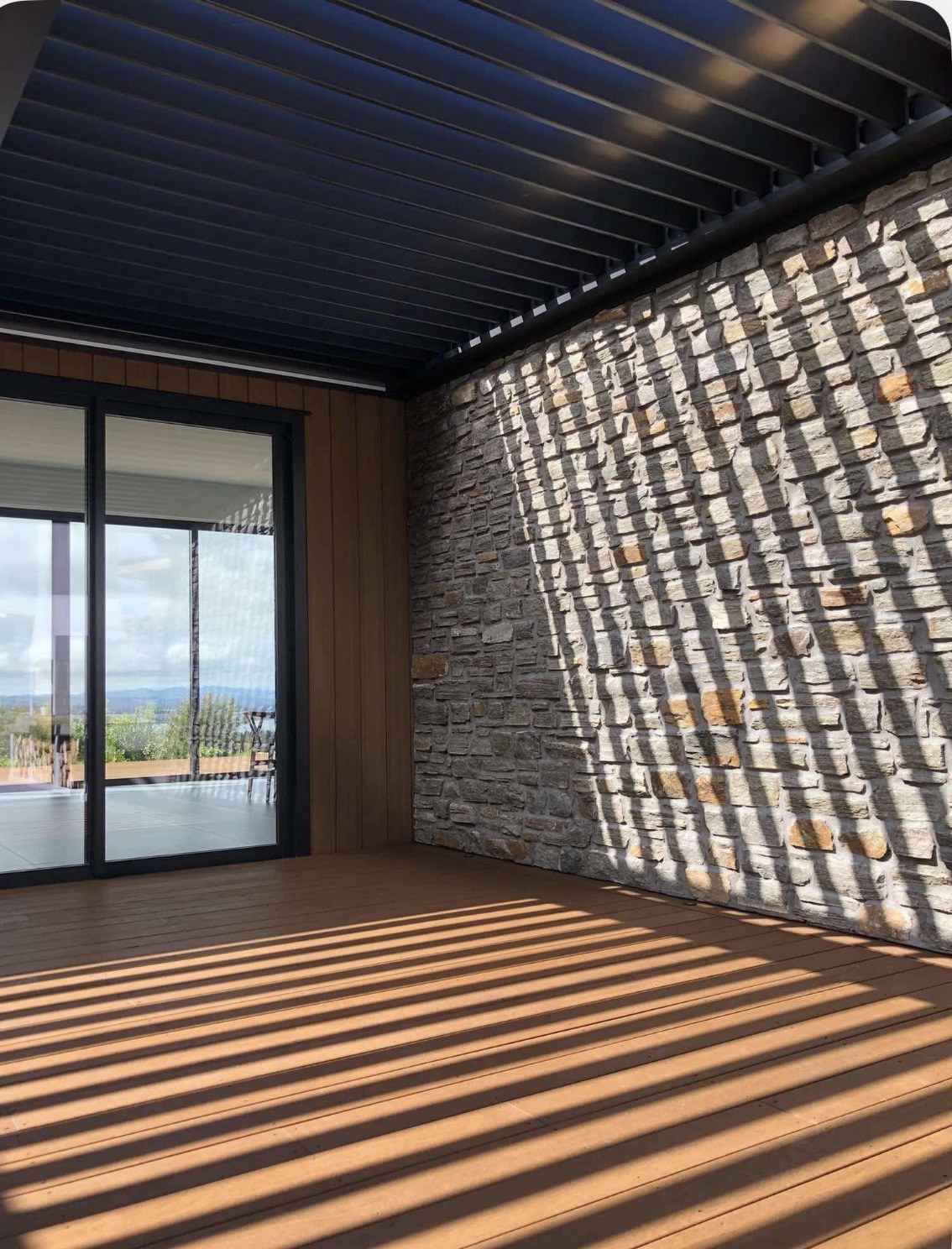 Open louvres casting shade patterns over the deck and stone wall