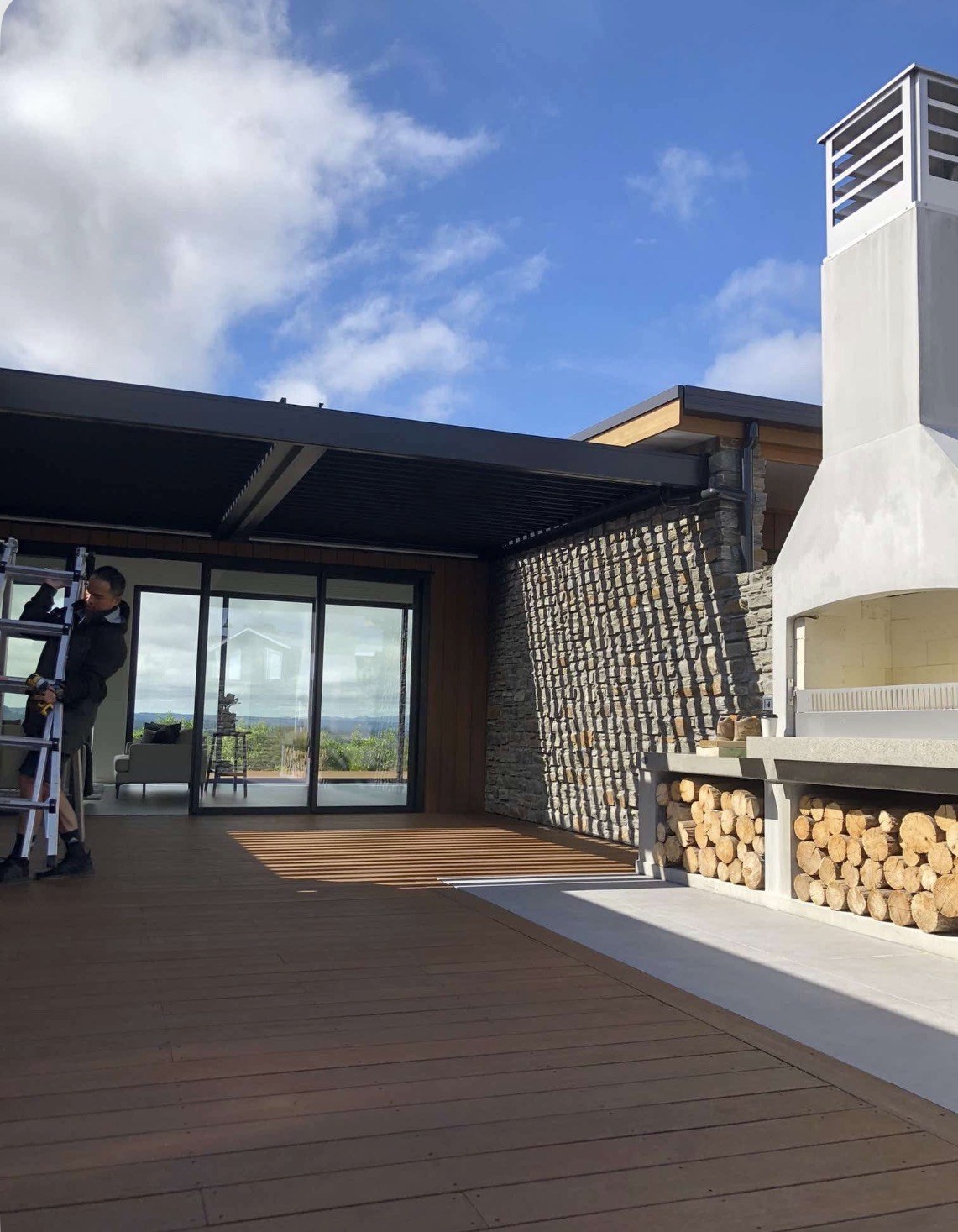 Motorised pergola installation in progress beside the stone wall and outdoor fireplace in Taupō
